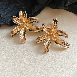 Close-up detail of large gold flower stud earrings with a hammered metal finish.