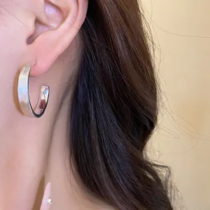 Dettaglio di un orecchino a cerchio a forma di C in argento spazzolato opaco indossato sull'orecchio
