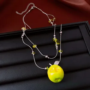 Detailaufnahme einer silbernen Halskette mit grünem Apfelanhänger und gelben Perlen.