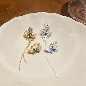 Détail des boucles d'oreilles papillon or et argent avec émail bleu sur une assiette blanche.