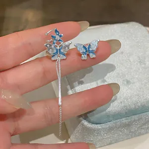 Détail d'une boucle d'oreille papillon en émail bleu avec gland en argent et fleur