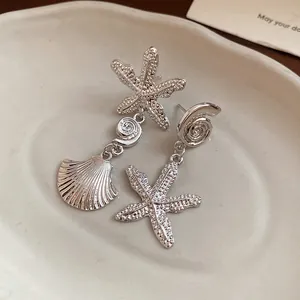 Close-up of silver-toned asymmetric starfish and shell drop earrings on a white plate.
