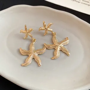 Detailed close-up of textured golden starfish dangle earrings on a white ceramic tray
