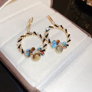 Nahaufnahme eleganter Goldreifenohrringe mit bunten Kristallperlen und hängenden Steinen