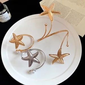 Elegant metal starfish arm cuff bracelets with pearl accents displayed on a white plate