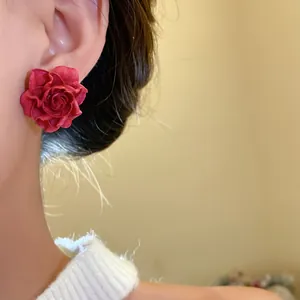 Close-up of elegant red rose flower stud earrings worn on ear, detailed petal texture