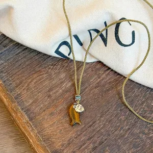 Close-up of artistic stone fish pendant and engraved heart charm on woven rope necklace