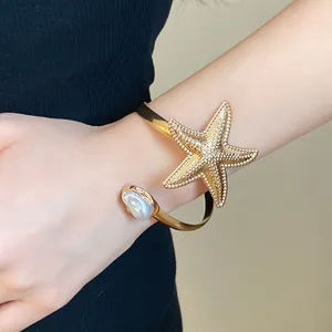 Detail of a vintage gold starfish arm cuff bracelet with a pearl on a model's arm.