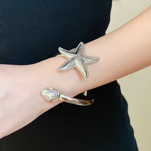 Detailed view of a silver starfish arm cuff with a baroque pearl on a female arm.