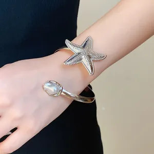 Macro detail of a vintage silver starfish cuff bangle with pearl on woman's wrist
