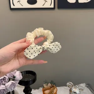 Detail shot of a delicate cream cloth hair scrunchie featuring a polka dot bow and pearl accent