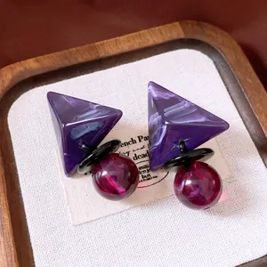 Detalle de pendientes retro de resina con triángulo púrpura y esfera de mármol magenta.