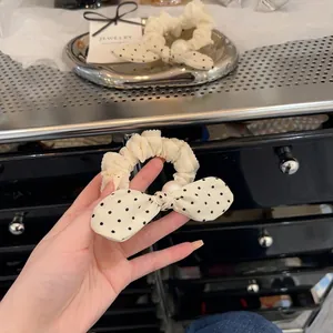 Close-up of a polka dot bow scrunchie with pearl detail and ruffled fabric edges.