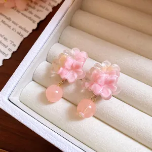 Dettaglio macro di orecchini a perno con fiori in resina rosa e perline in un portagioie