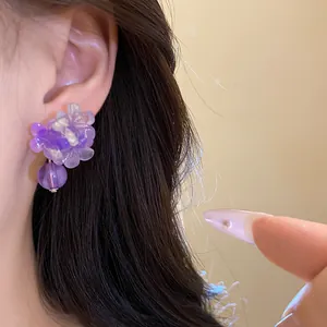 Primo piano di eleganti orecchini a fiore in resina viola indossati sull'orecchio di una modella