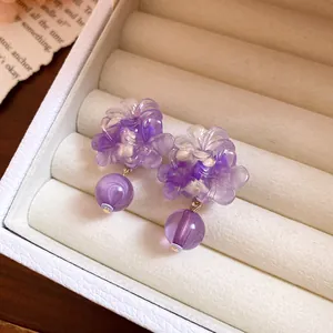 Primo piano di orecchini a fiore in resina viola in un portagioie beige crema.
