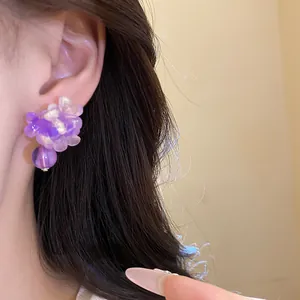 Dettaglio di un orecchino a lobo a fiore in resina viola con perla viola sul lobo