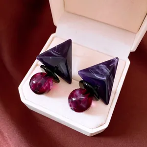 Primer plano de pendientes geométricos de resina con triángulo púrpura y cuenta redonda.