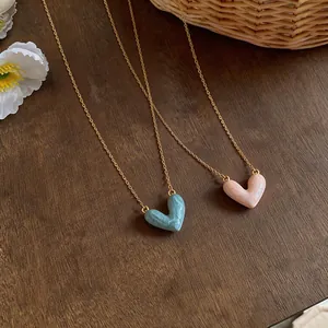 Detail view of two 14k real gold plated oil-drop heart necklaces on a wooden surface
