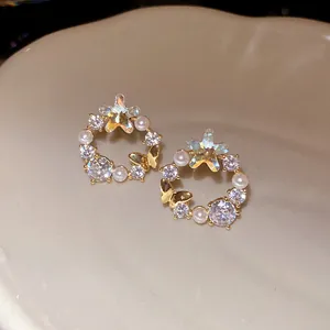 Close-up of 18k gold plated stud earrings with pearls, zircons and butterfly charm