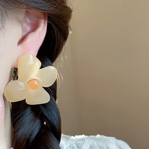 Detailed close-up of retro cream resin flower earring with orange bead center on ear