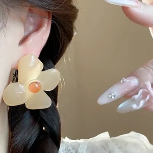 Detailed close-up of a large resin flower stud earring in pale yellow on model's ear
