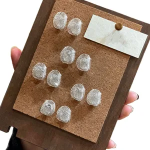 Minimalist hollow oval silver stud earrings displayed on a rustic wooden cork board