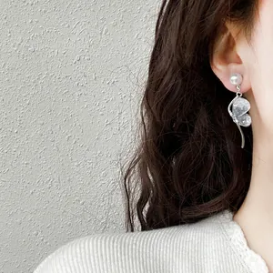 Close-up of elegant crystal butterfly and pearl drop earrings on a model's ear.