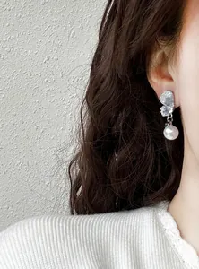 Detail shot of a silver-tone crystal butterfly earring with a dangling white pearl charm.