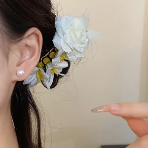 Close-up of a floral hair pin with white petals and a pearl earring worn by a model.