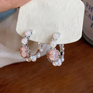 Detailed close-up of C-shaped silver earrings with pink flower and white pearls