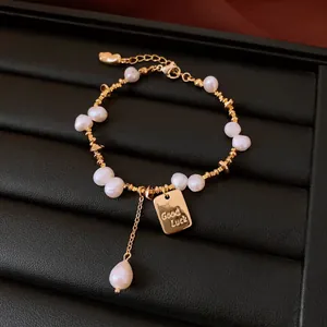 Detail shot of a gold-plated bracelet featuring baroque pearls and a Good Luck tag.