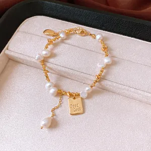 Detailed macro shot of an 18K gold-plated bracelet featuring pearls and a 'Good Luck' pendant.