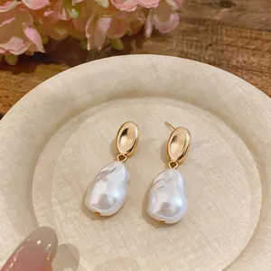 Close-up of elegant gold stud earrings with irregular white baroque pearls on a dish.