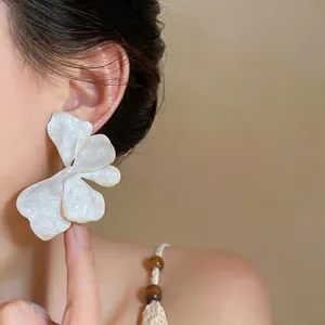 Close-up detail of white oil-drip flower stud earrings with elegant gold-rimmed edges
