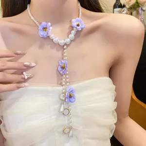 Detail view of a pearl beaded necklace with purple chiffon flowers worn by a model