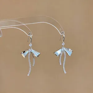 Dettaglio orecchini a fiocco in argento con nastri pavé scintillanti su un supporto.