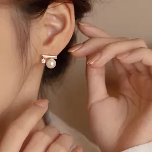 Close-up view of minimalist gold bar earring featuring a pearl and zircon on model