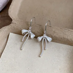 Dettaglio ravvicinato di eleganti orecchini a fiocco in argento con zirconi e smalto bianco