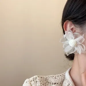 Dettaglio di grandi orecchini a fiore in tulle bianco indossati per uno stile trendy.