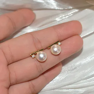 Close-up detail of minimalist white pearl and zircon stud earrings held on a hand