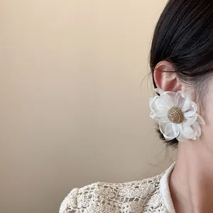 Primo piano dettagliato di un grande orecchino a fiore in rete bianca indossato da modella.