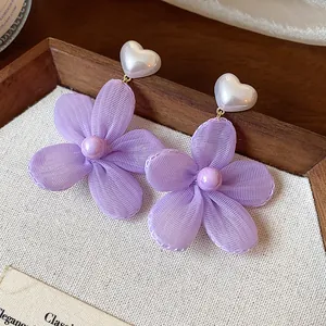 Primo piano di orecchini a fiore in chiffon lavanda con perle bianche a cuore.