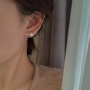 Close-up view of elegant zircon and pearl stud earrings worn by a model in a minimalist style