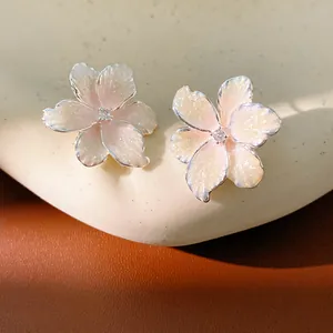 Close-up of pink enamel flower stud earrings with zircon centers on a natural stone prop