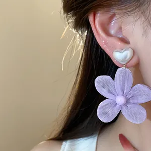 Dettaglio orecchini a fiore in chiffon viola con perla a forma di cuore indossati.