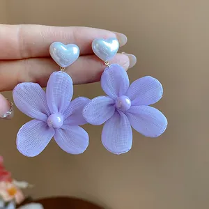 Primo piano dettagliato di orecchini a fiore in chiffon lavanda con cuori di perla bianca.