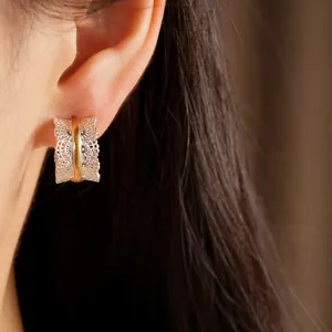 Primer plano detallado de elegantes pendientes en forma de C de encaje bicolor en una oreja