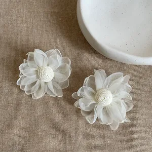 Dettaglio di grandi orecchini a fiore in rete bianco sporco su lino beige