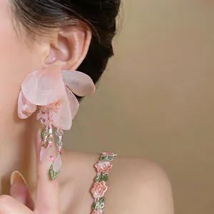 Close-up detail of pink fabric flower earrings with beaded tassels on model
